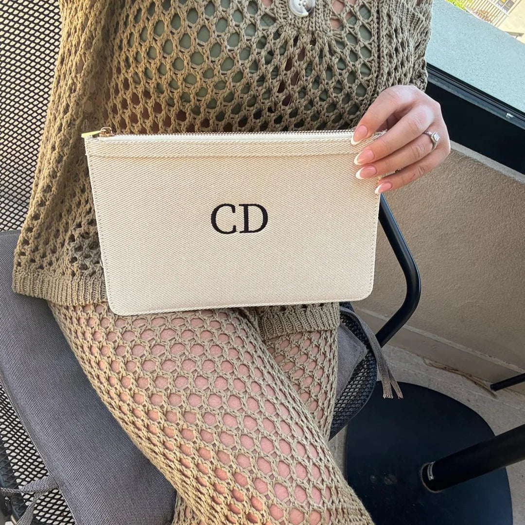 Person holding a beige pouch with initials 'CD' in a vehicle.