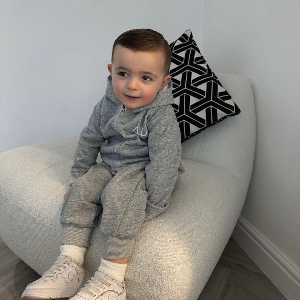 Child sitting on a white chair with a black and white patterned pillow in a minimalistic room.
