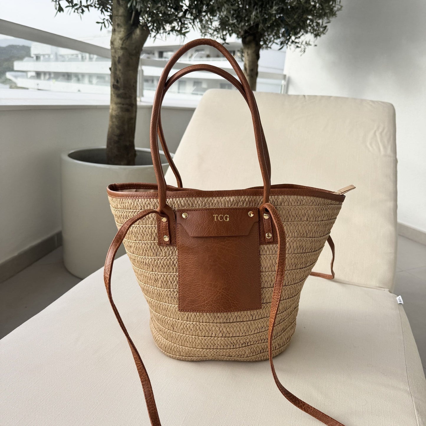 Woven bag with brown leather accents on a white chair outdoors