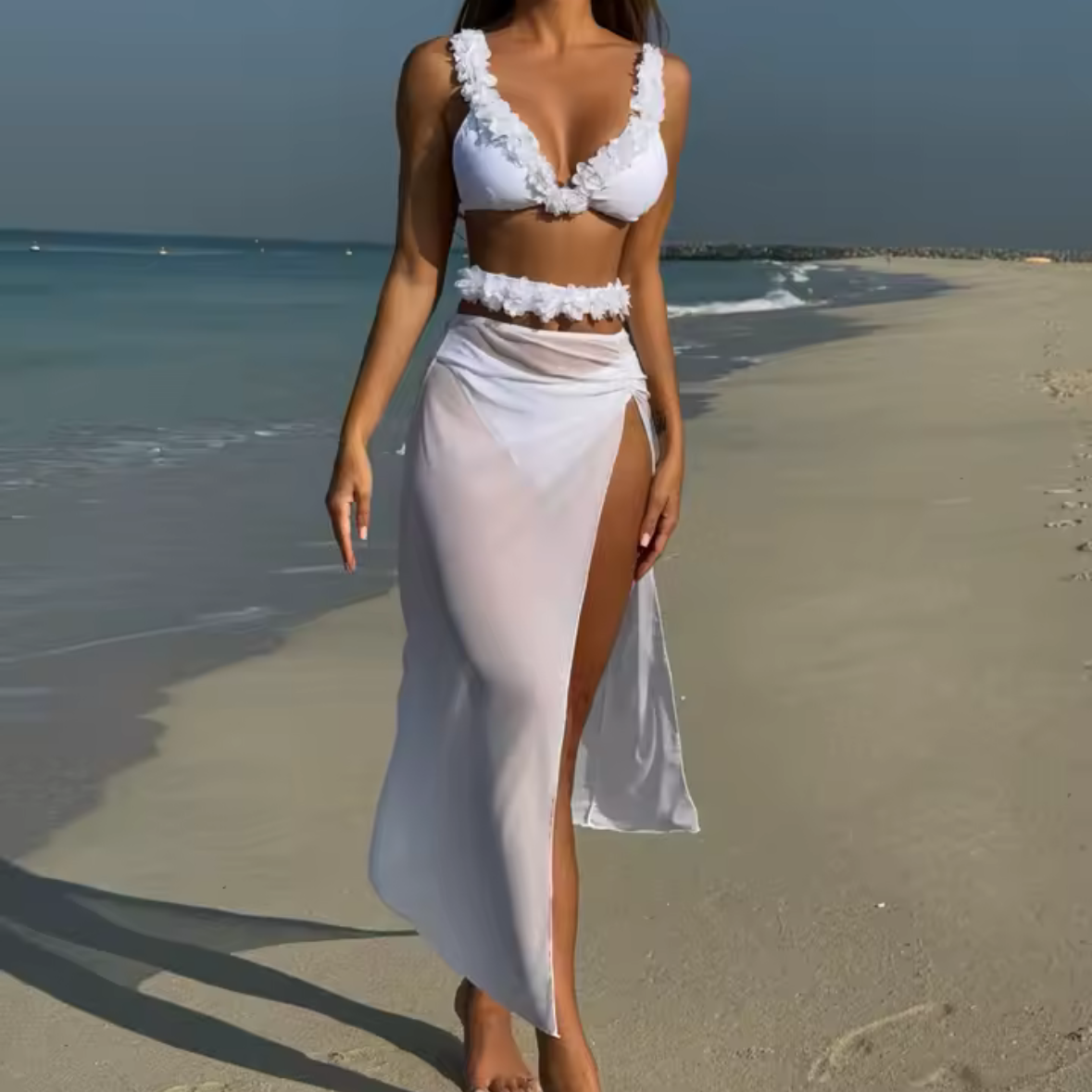 Woman in a white outfit walking on a beach with a clear sky.