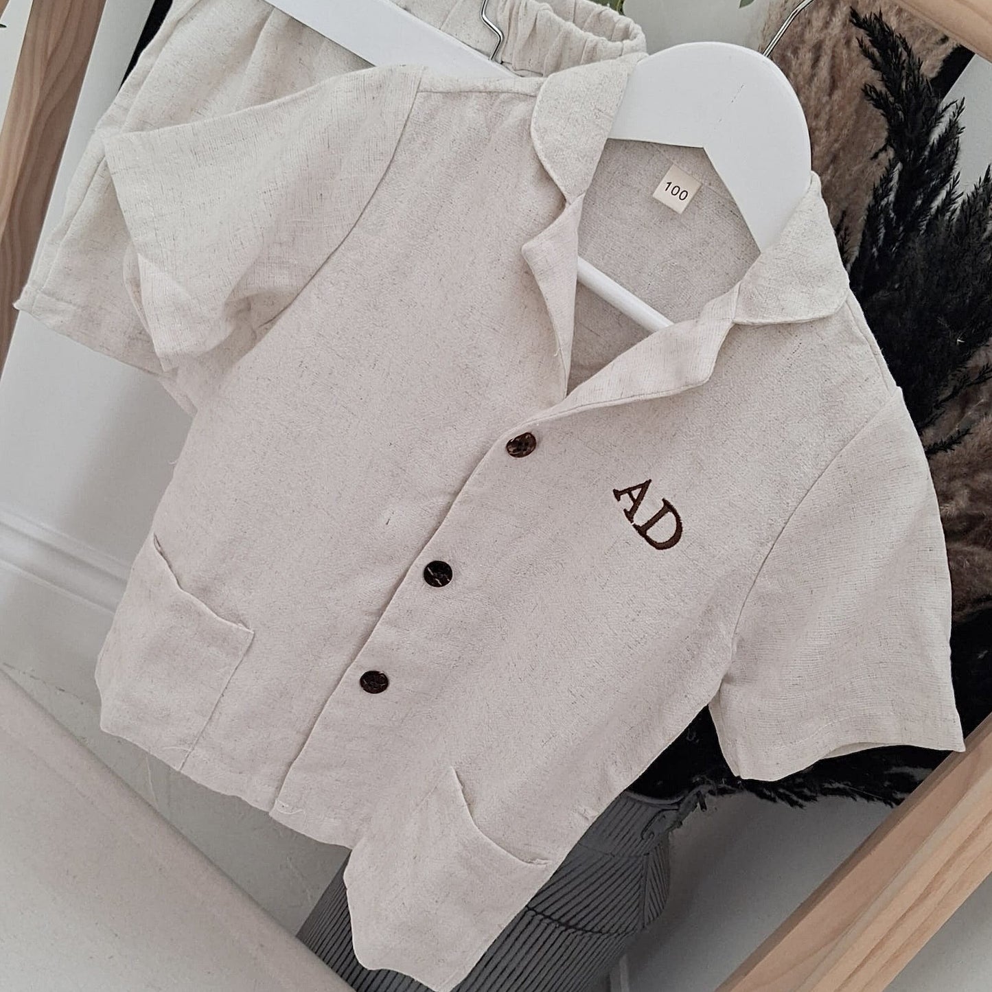 Beige blazer with 'AD' monogram on a hanger against a neutral background