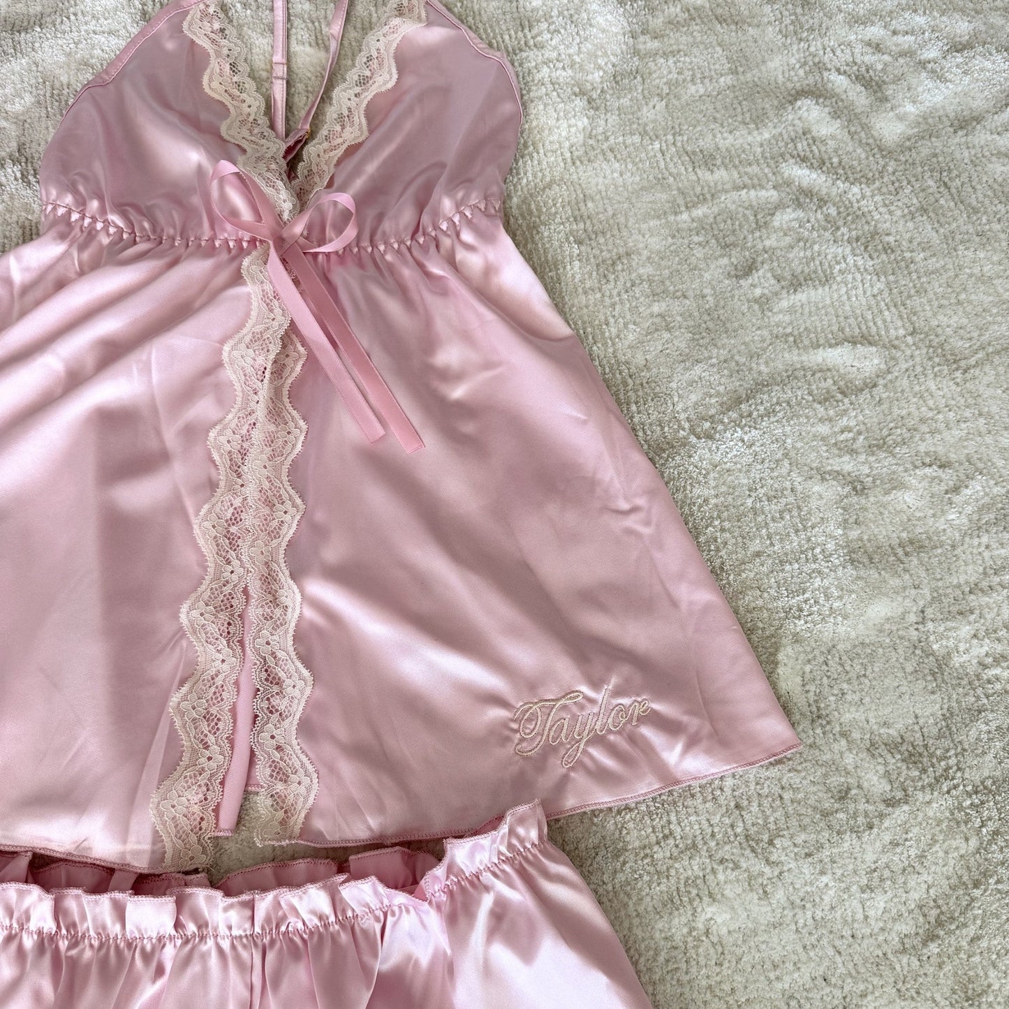 Pink satin pyjamas with lace details on a textured beige surface