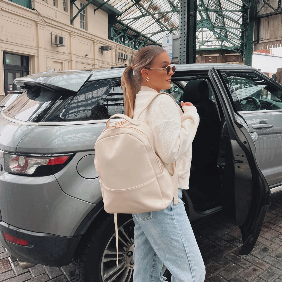 Woman with a beige backpack standing next to an open car door