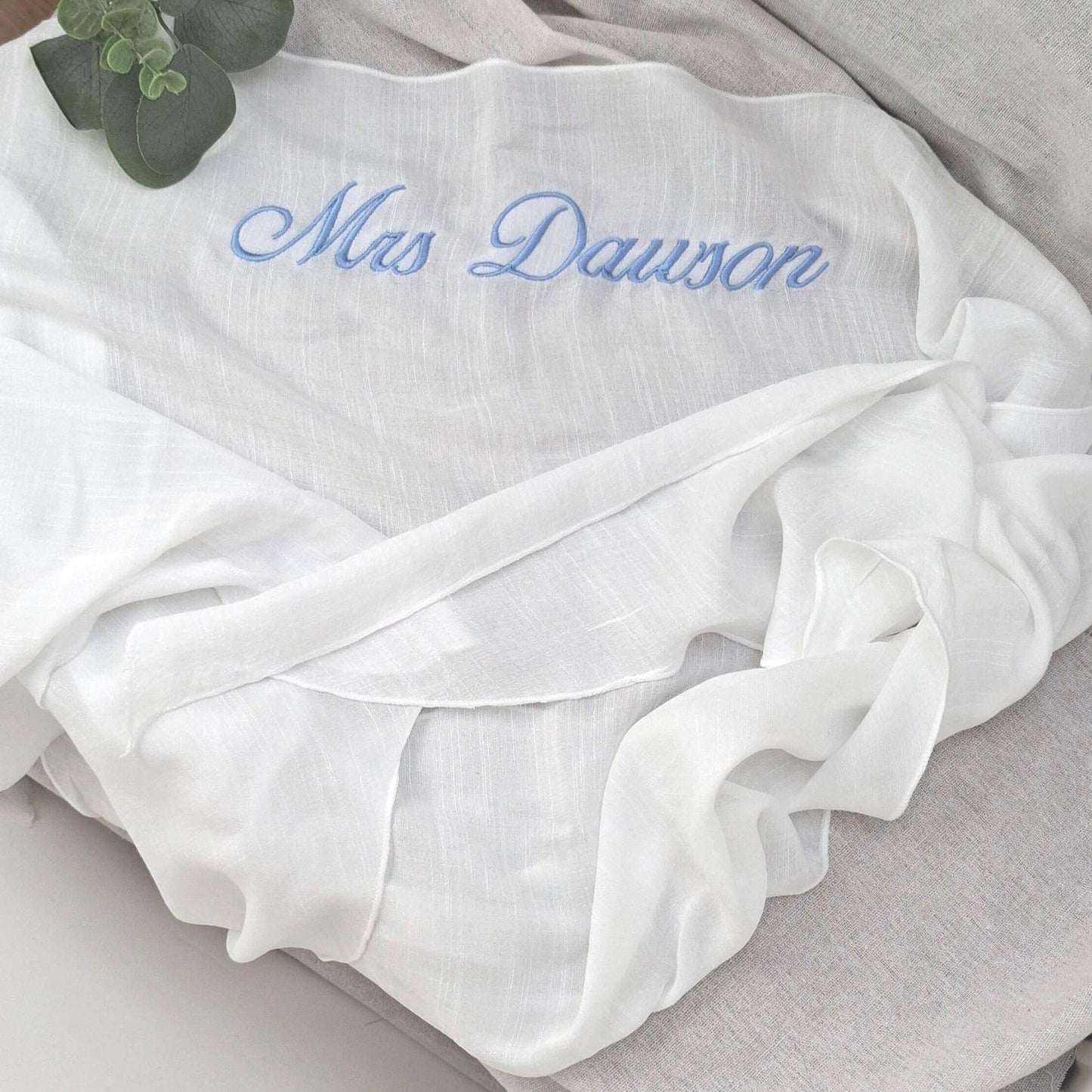 White sarong with 'Mrs Dawson' embroidered in blue on a light gray surface.