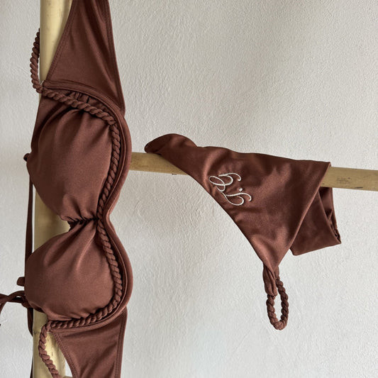 Brown bikini set with ruched design on a wooden stand against a white wall.