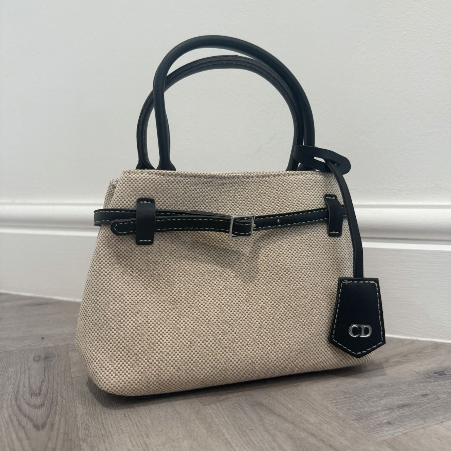 Beige handbag with black accents on a wooden floor against a white wall