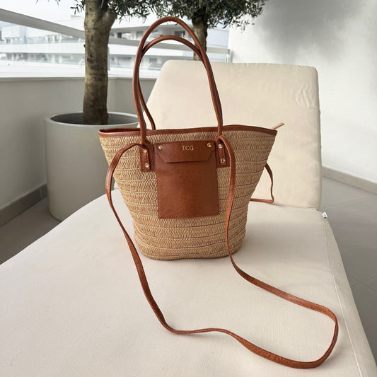 Woven handbag with leather accents on a white surface with a plant in the background
