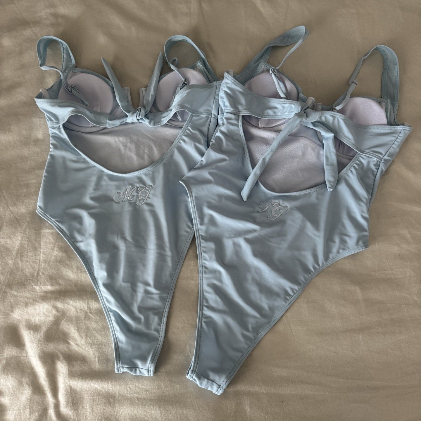 Light blue swimsuits with bow details on a beige fabric background