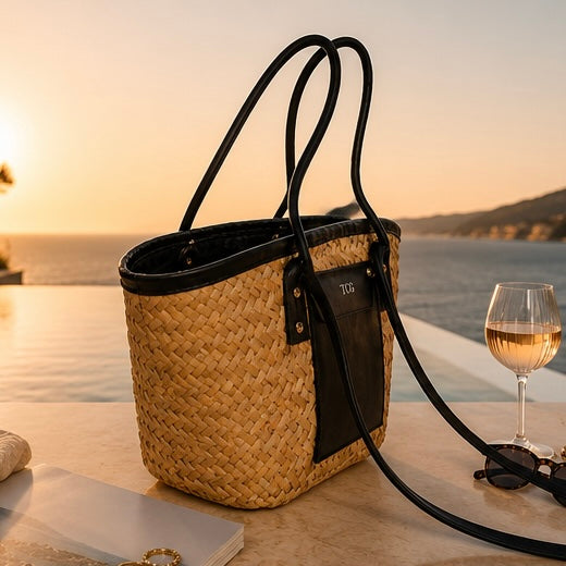 Woven bag with black accents on a table by a poolside at sunset