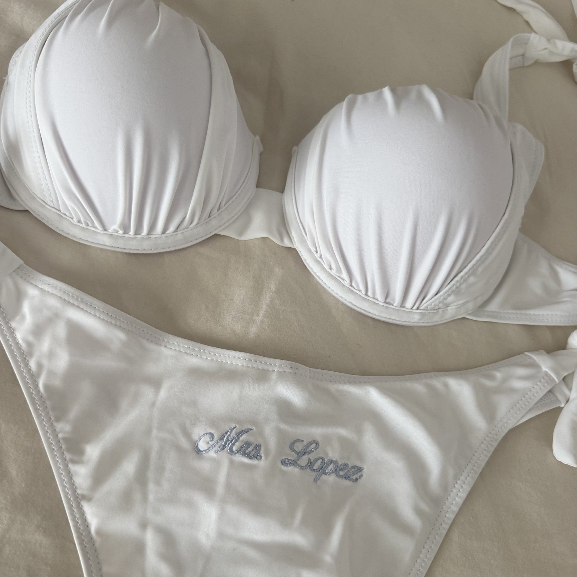 White bikini set with 'Miss Lopez' branding on a beige background