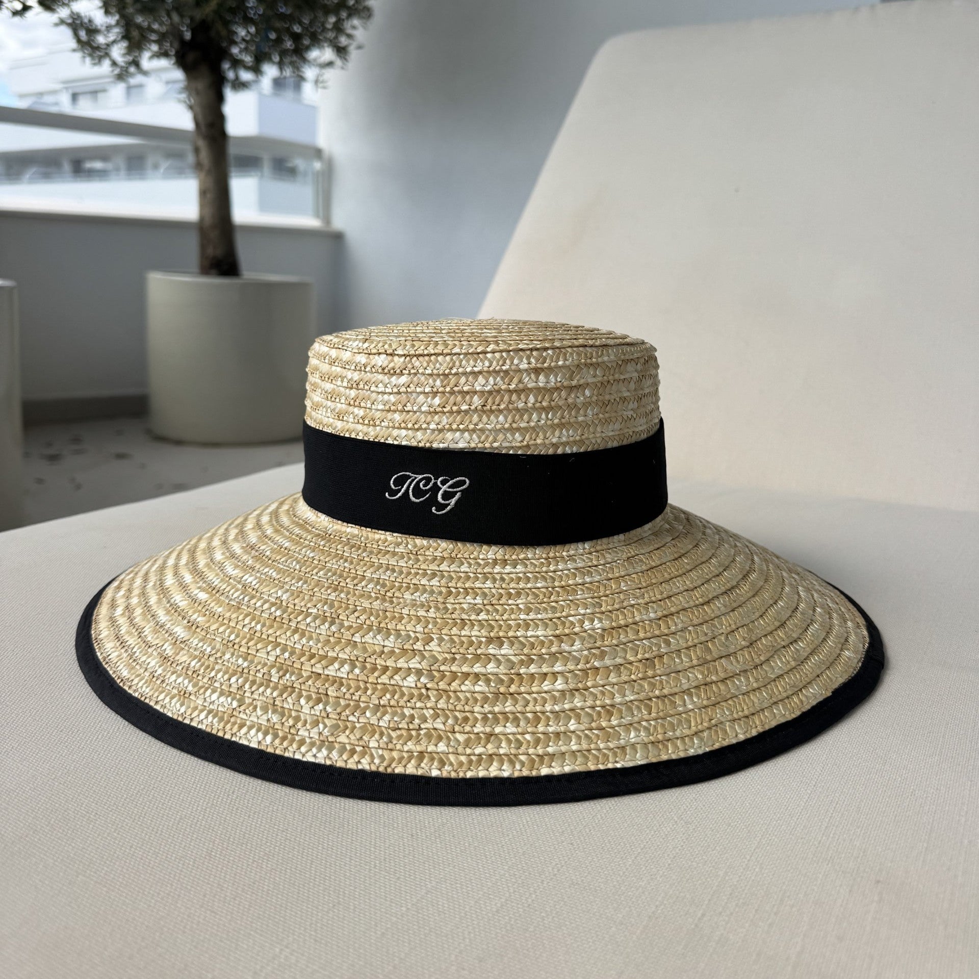 Straw hat with a black band on a white surface, with a blurred indoor background.