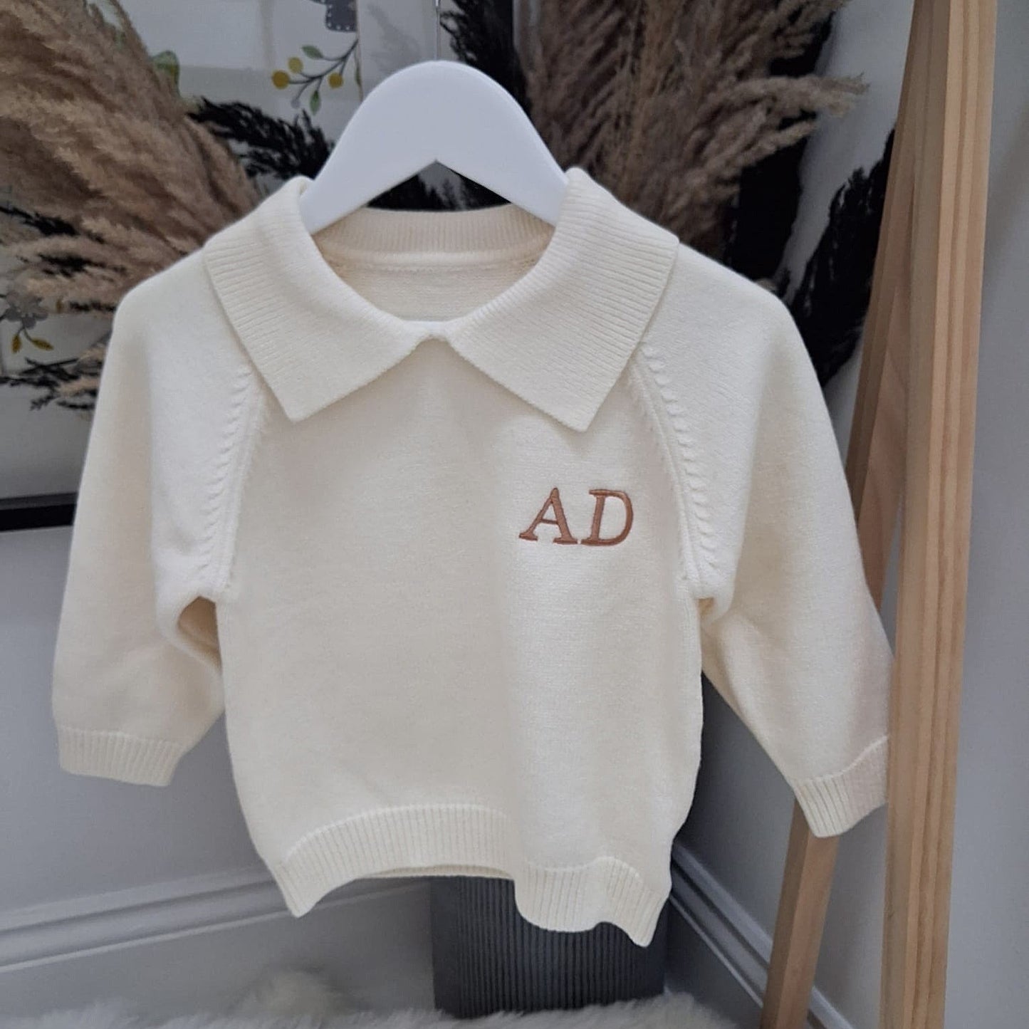 White sweater with 'AD' initials on a hanger against a neutral background