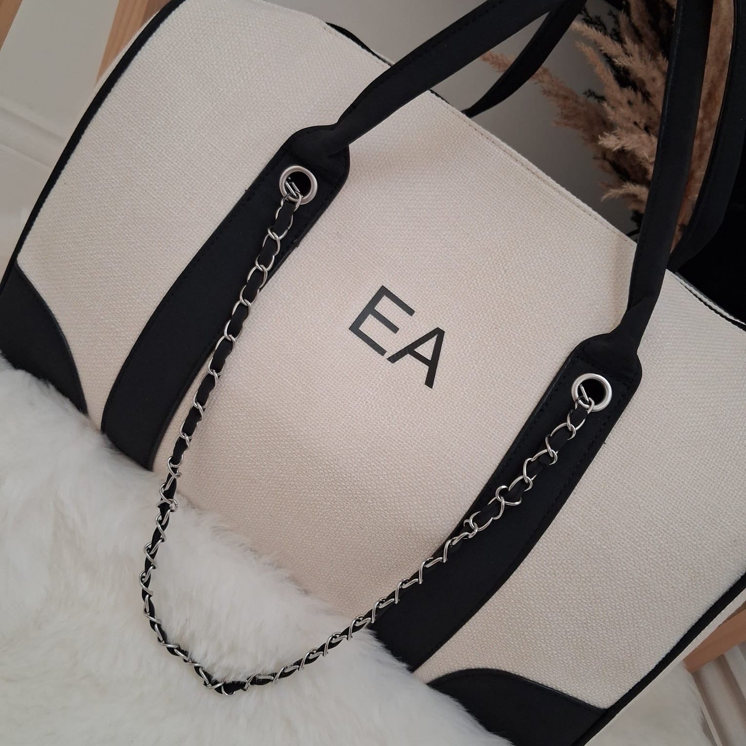 Beige tote bag with black accents and 'EA' monogram on a white surface.