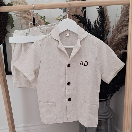 Beige short-sleeve shirt with 'AD' embroidery on a hanger against a neutral background.