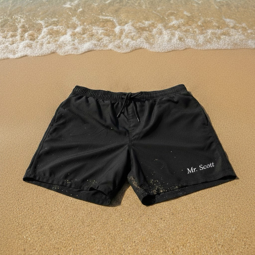 Black shorts with 'Mr. Scott' text on a sandy beach
