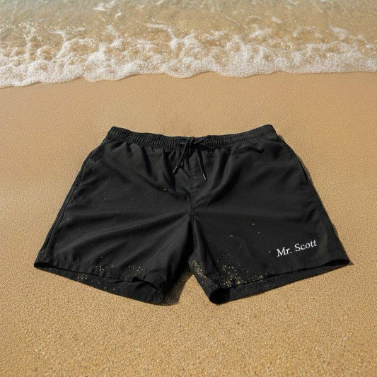 Black shorts with 'Mr. Scott' text on a sandy beach