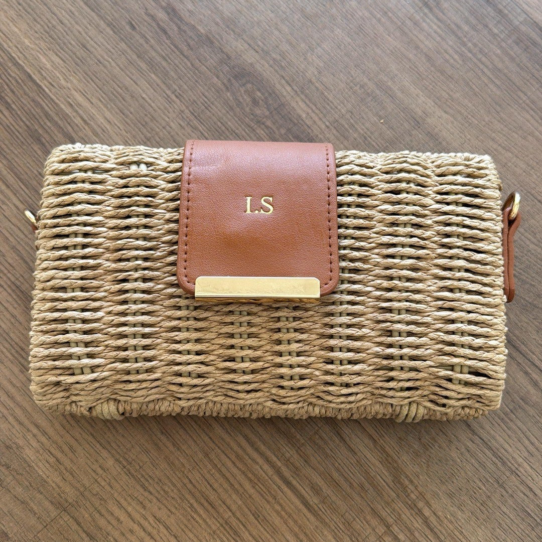 Wicker clutch bag with brown leather strap on a wooden surface