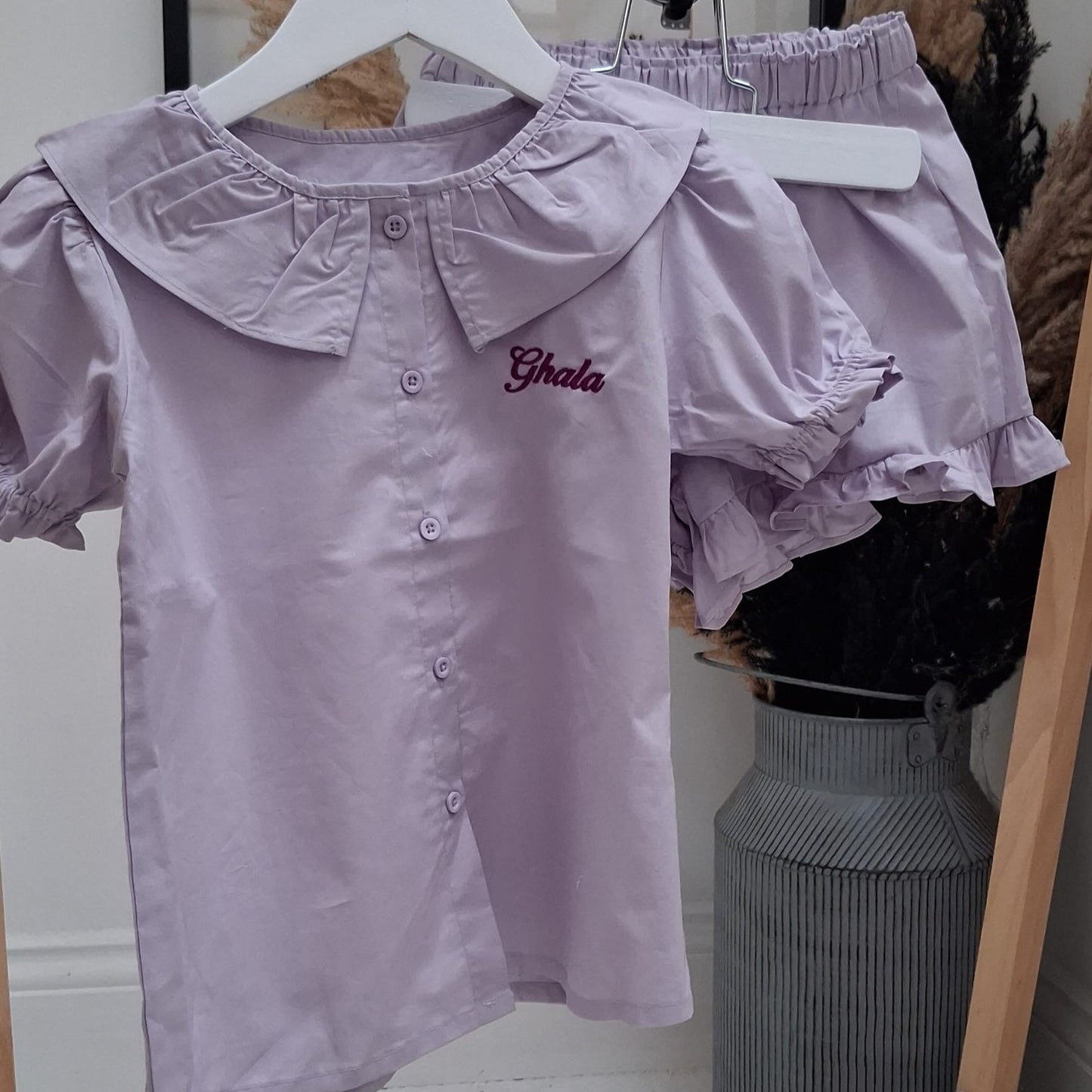 Light purple blouse with ruffled sleeves and collar on a hanger against a neutral background