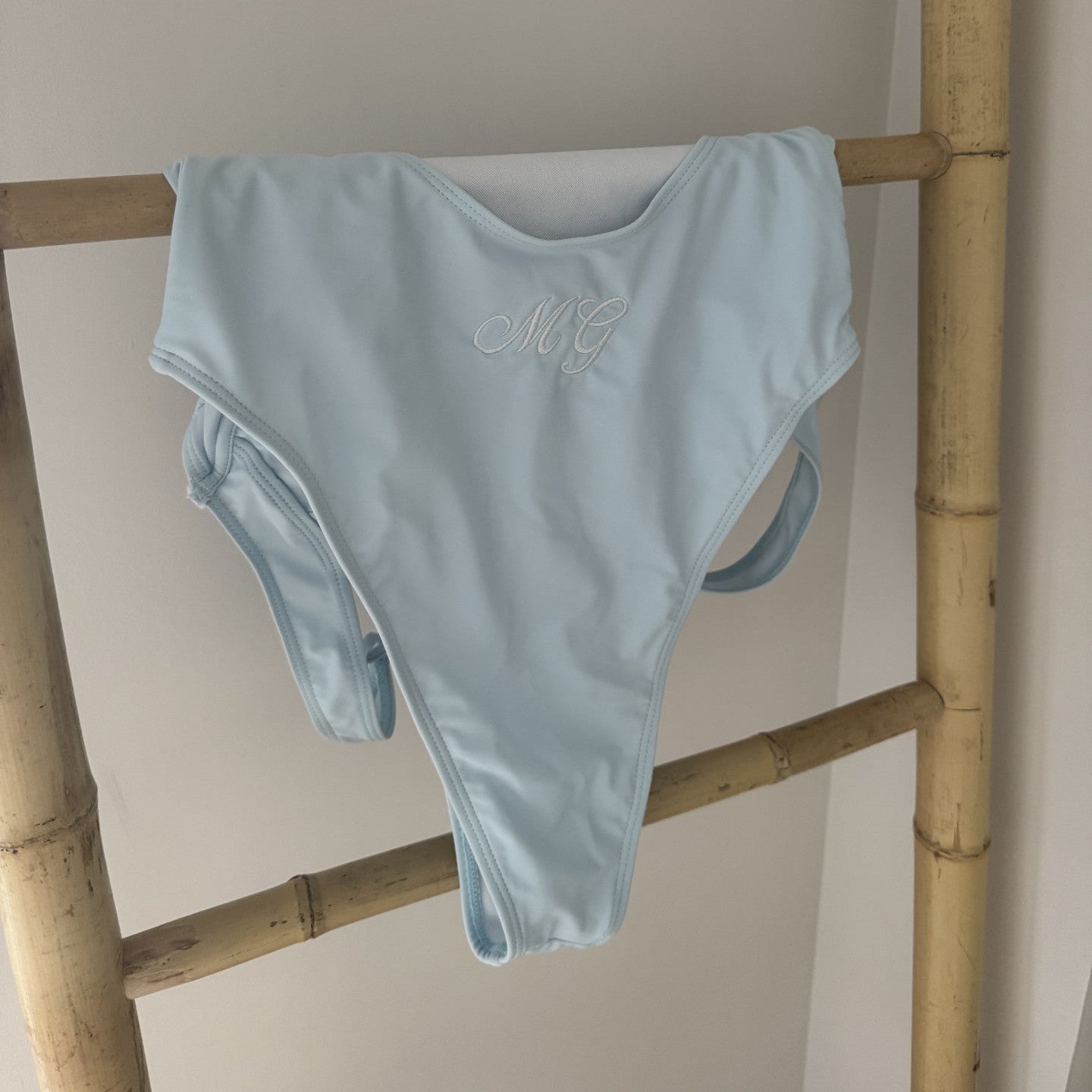 Light blue bikini hanging on a wooden rack against a plain wall.