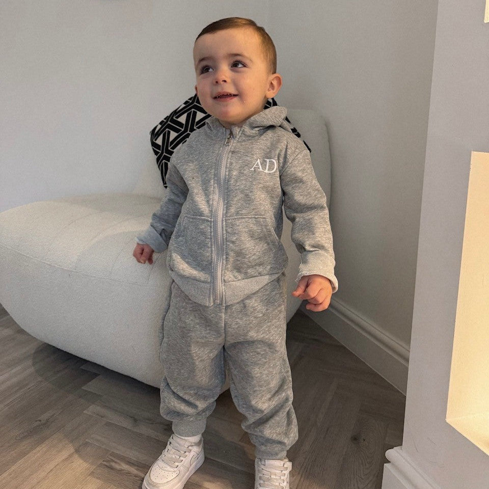 Child wearing a gray tracksuit with 'AD' logo in a room.