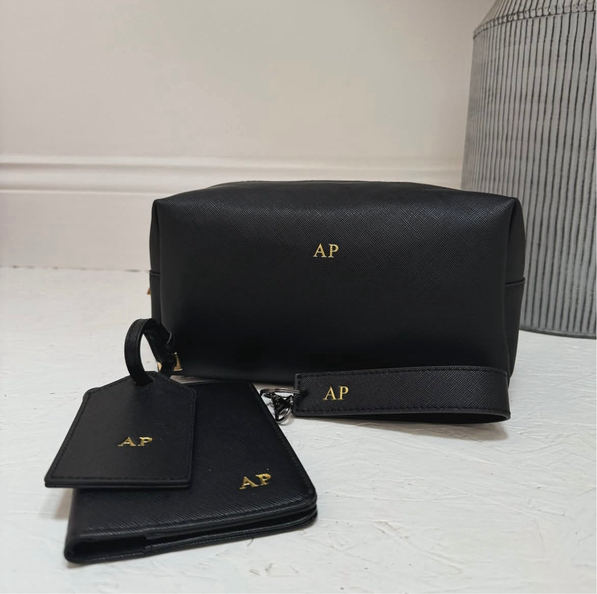 Black leather pouch set with gold initials on a white surface