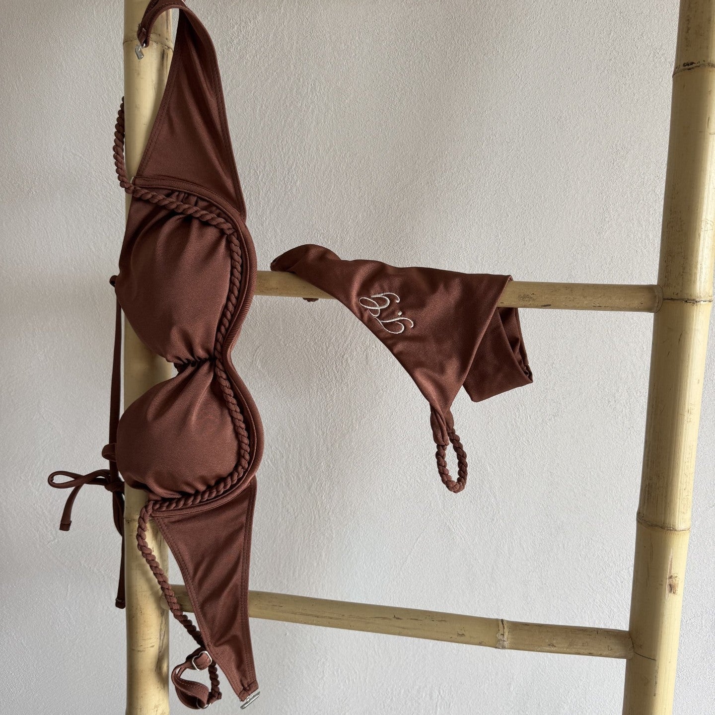 Brown bikini set hanging on a bamboo rack against a white wall