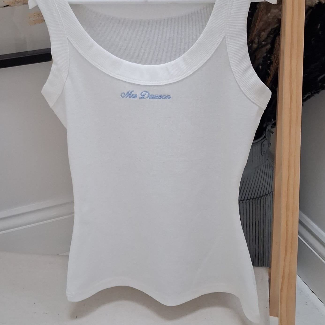 White tank top with embroidery on a hanger against a neutral background