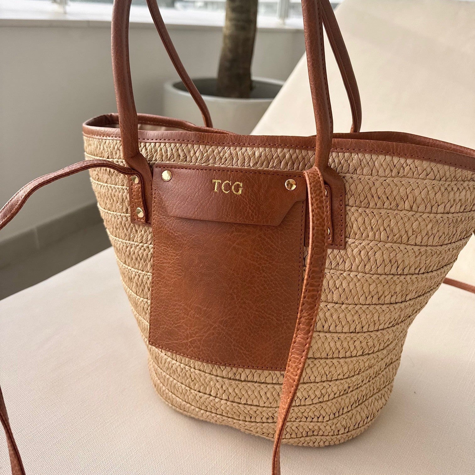 Woven handbag with brown leather accents on a surface with a blurred background