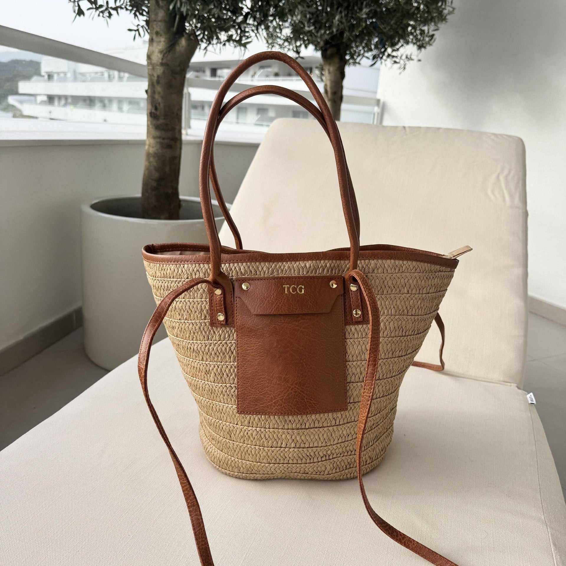 Woven bag with brown leather accents on a white chair outdoors
