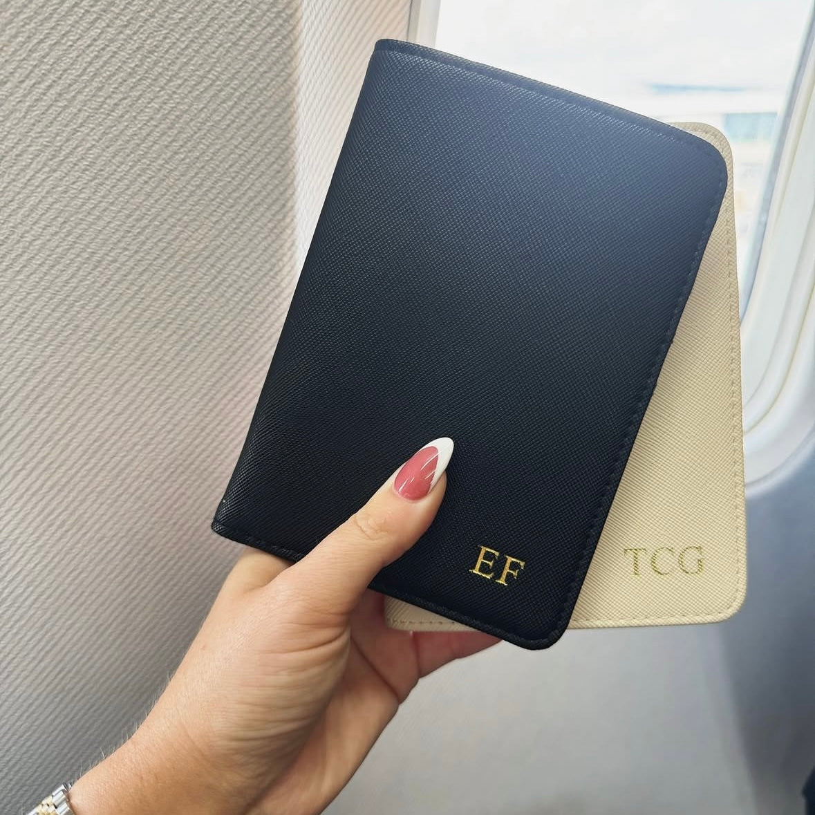 Hand holding a black passport holder with gold initials against a neutral background