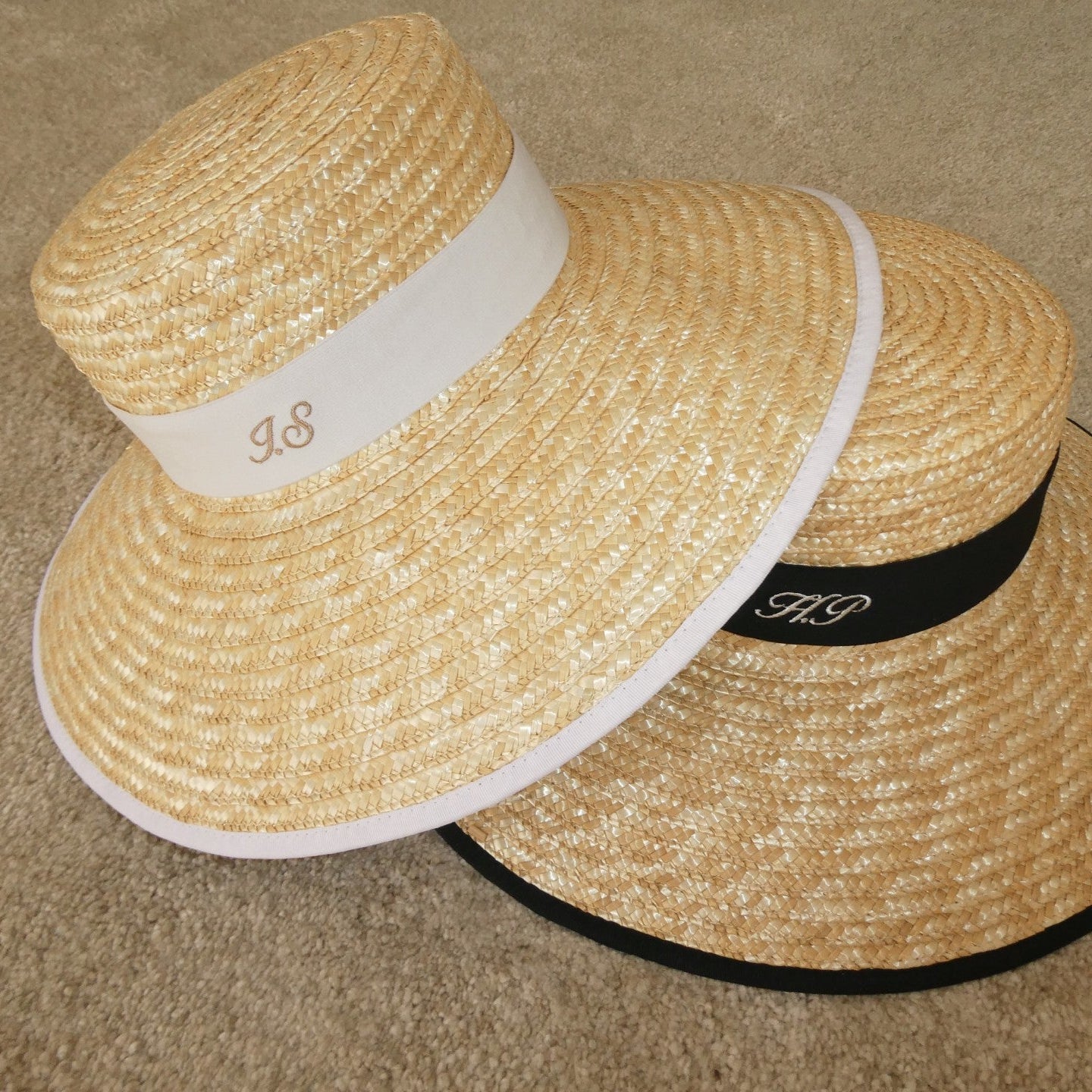 Two straw hats with branded bands on a beige carpet