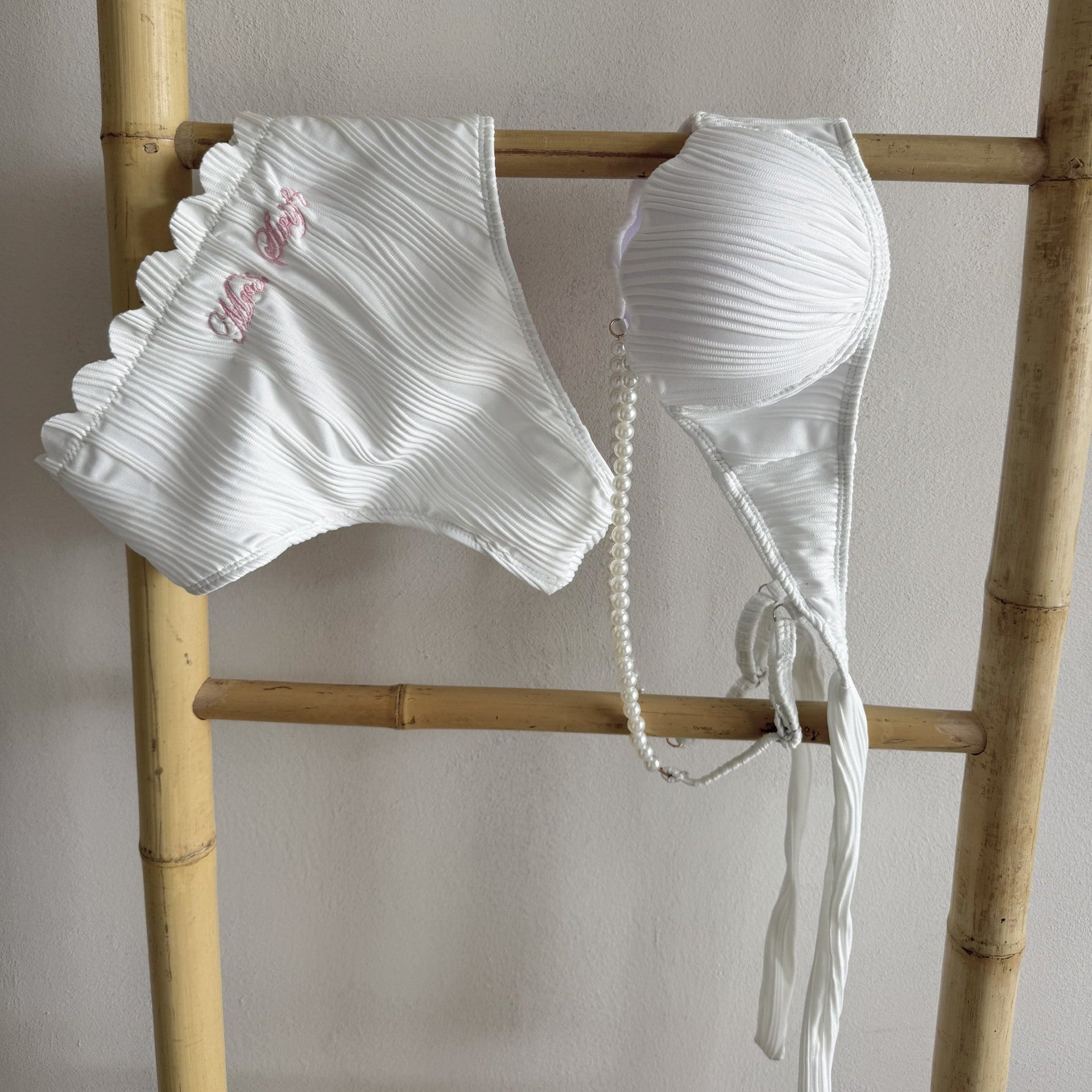 White bikini set on a wooden ladder against a plain background