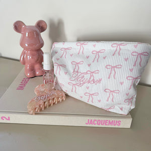 Pink bear figurine, hairbrush, and pouch on a book with 'Jacquemus' branding. with personalised bag