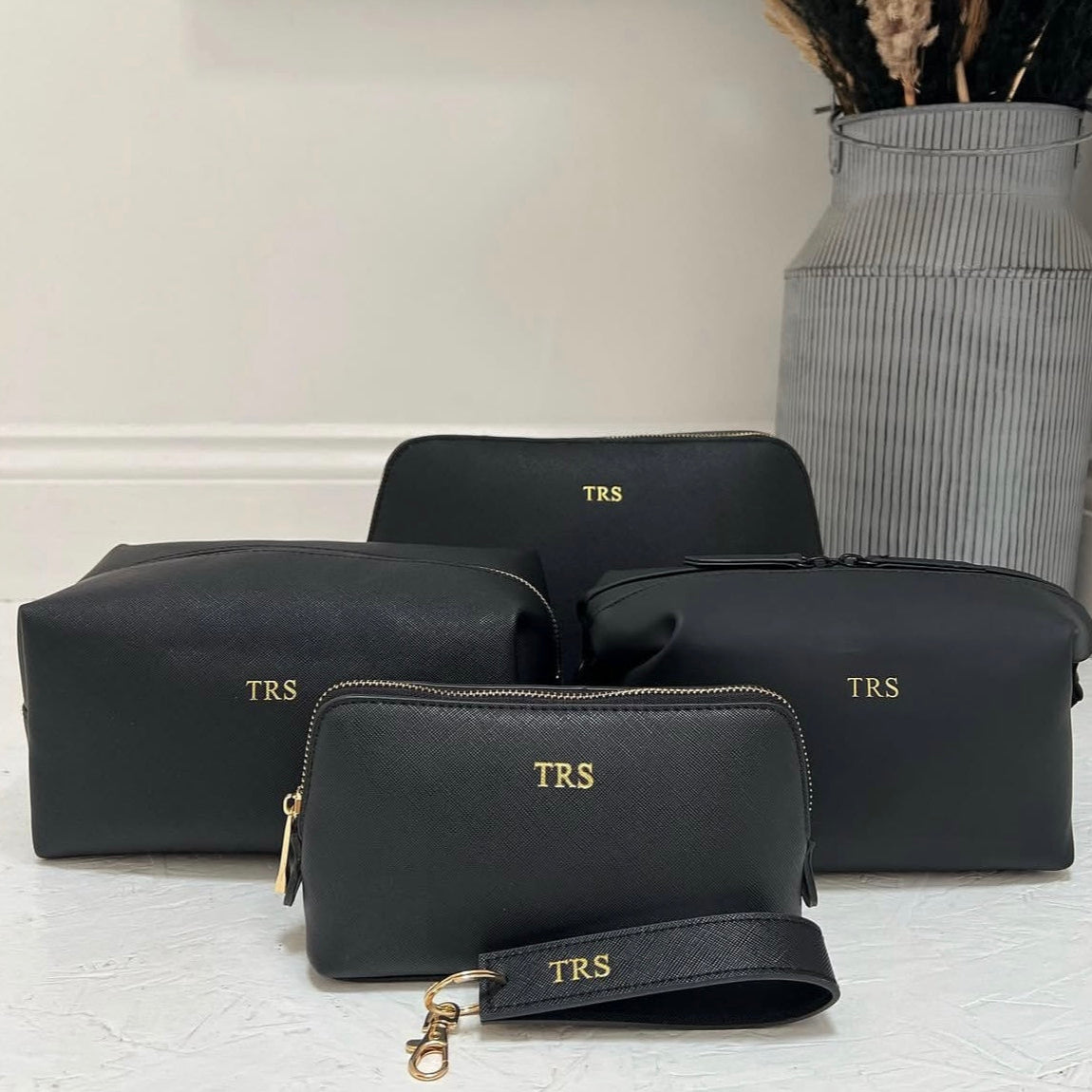 Set of black cosmetic bags with 'TRS' monogram on a light background
