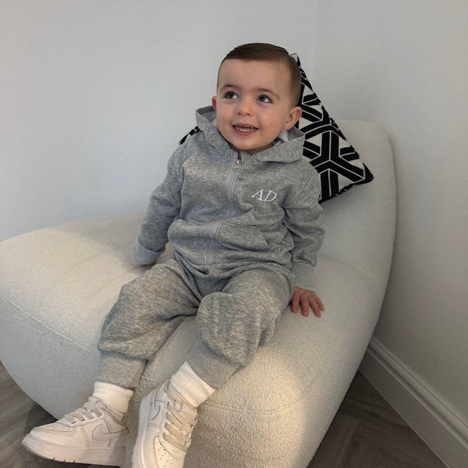 Child wearing a gray tracksuit with a logo, sitting on a white couch.