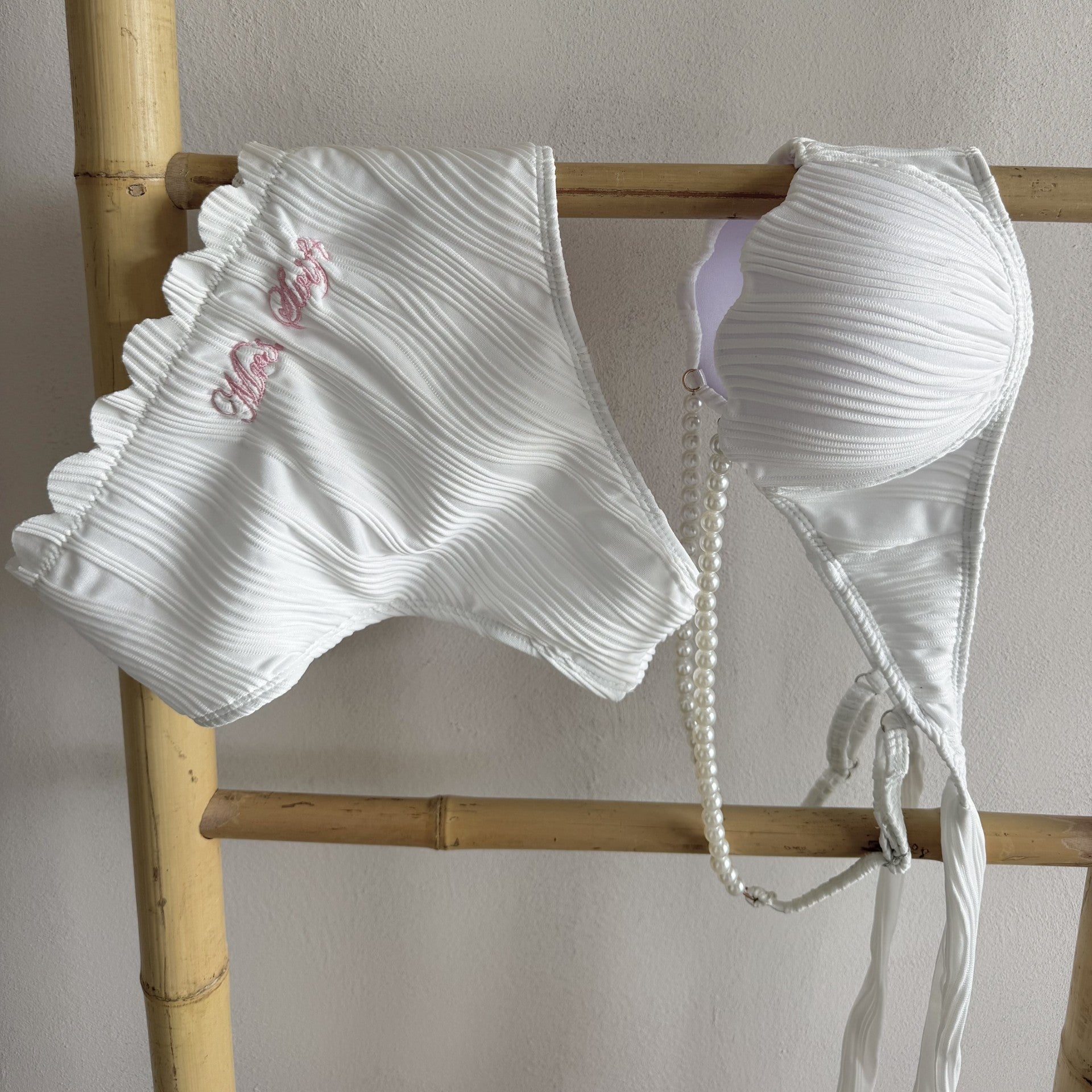 White bikini set with ruffled details on a wooden rack against a neutral background