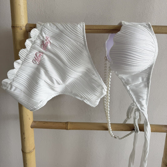 White bikini set with ruffled details on a wooden rack against a neutral background