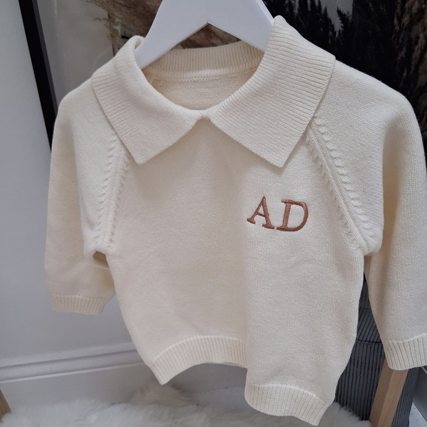Beige knitted vest with 'AD' embroidery on a white hanger.