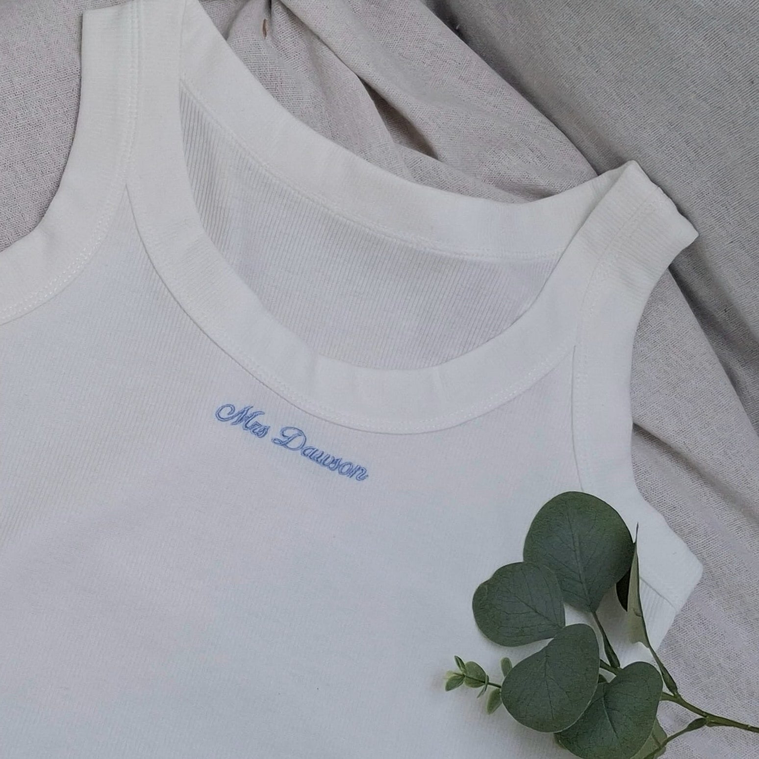 White tank top with blue text on a light gray background