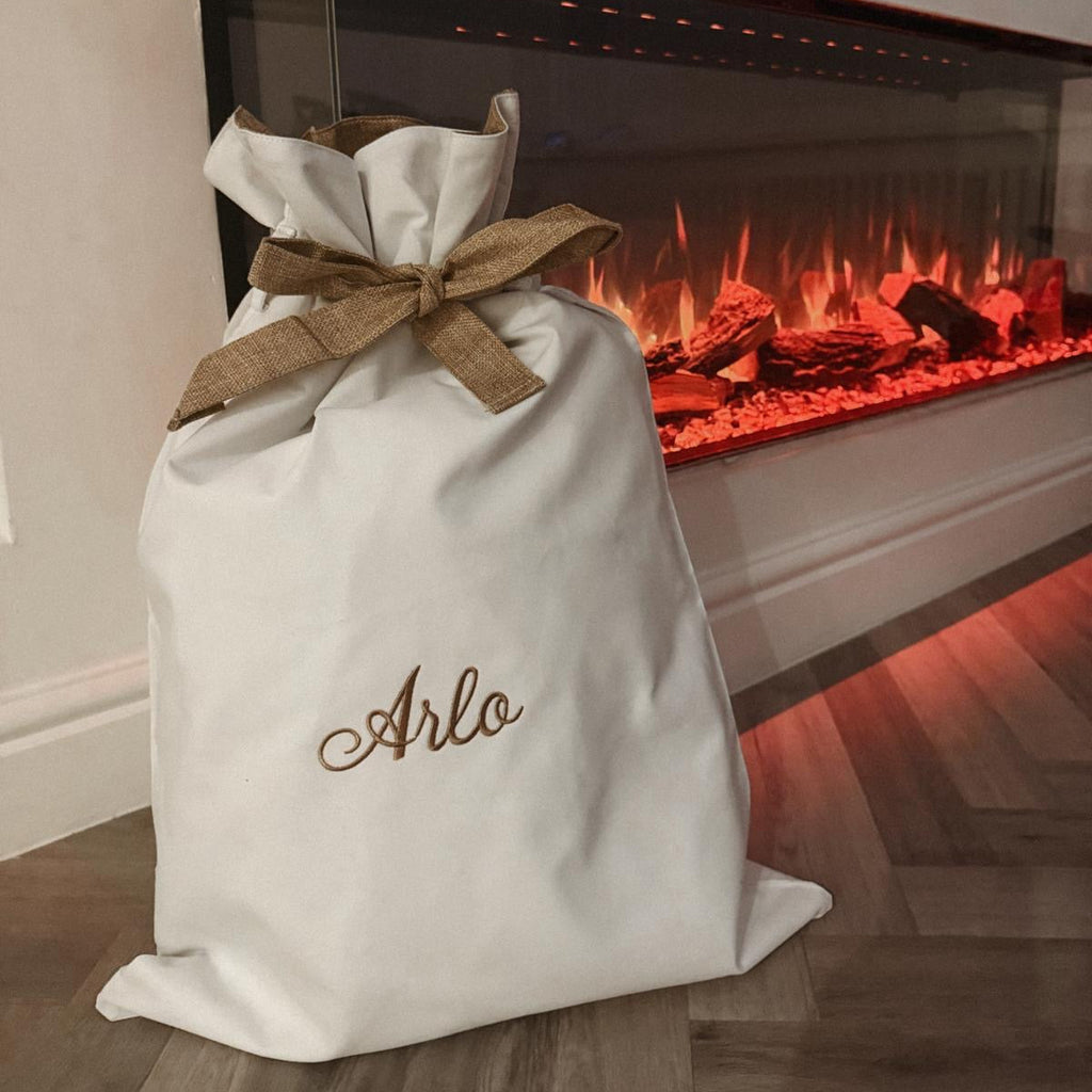 White sack with a brown bow labeled 'Arlo' in front of a lit fireplace.