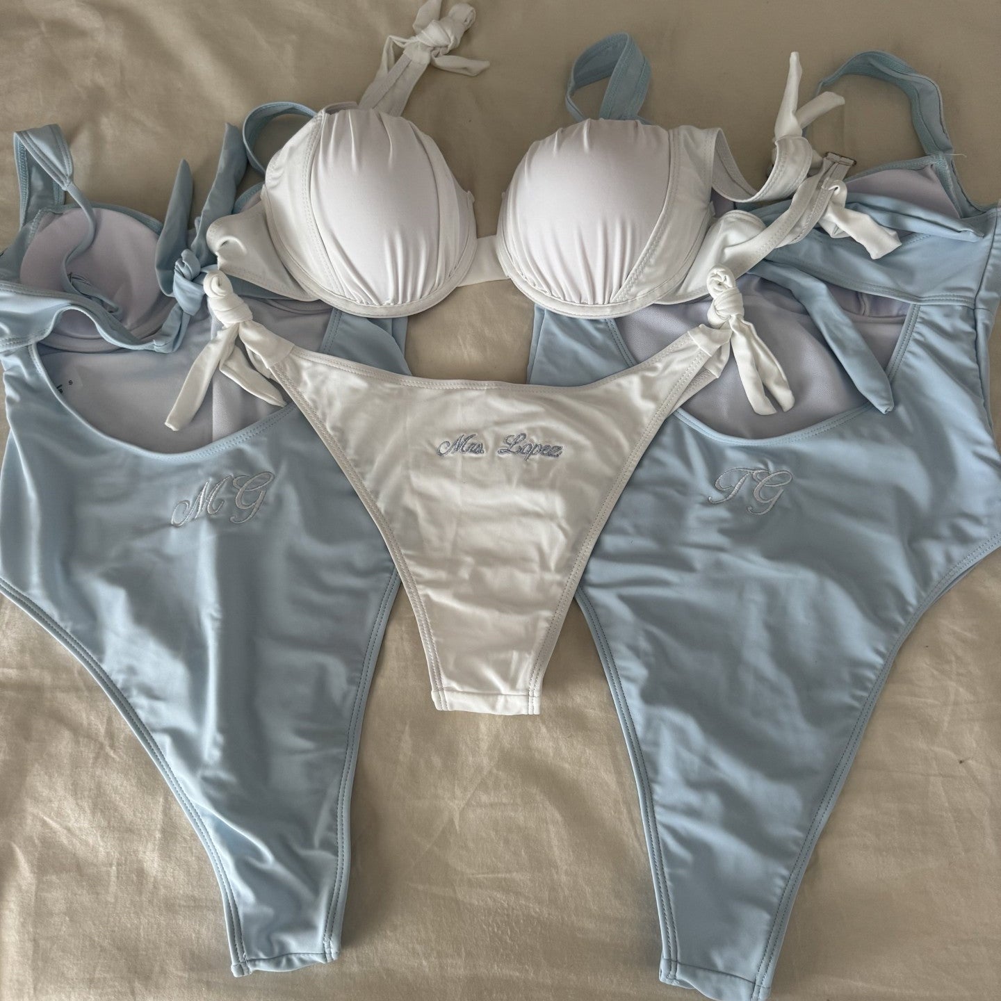 White bikini with light blue swimsuits on a beige surface