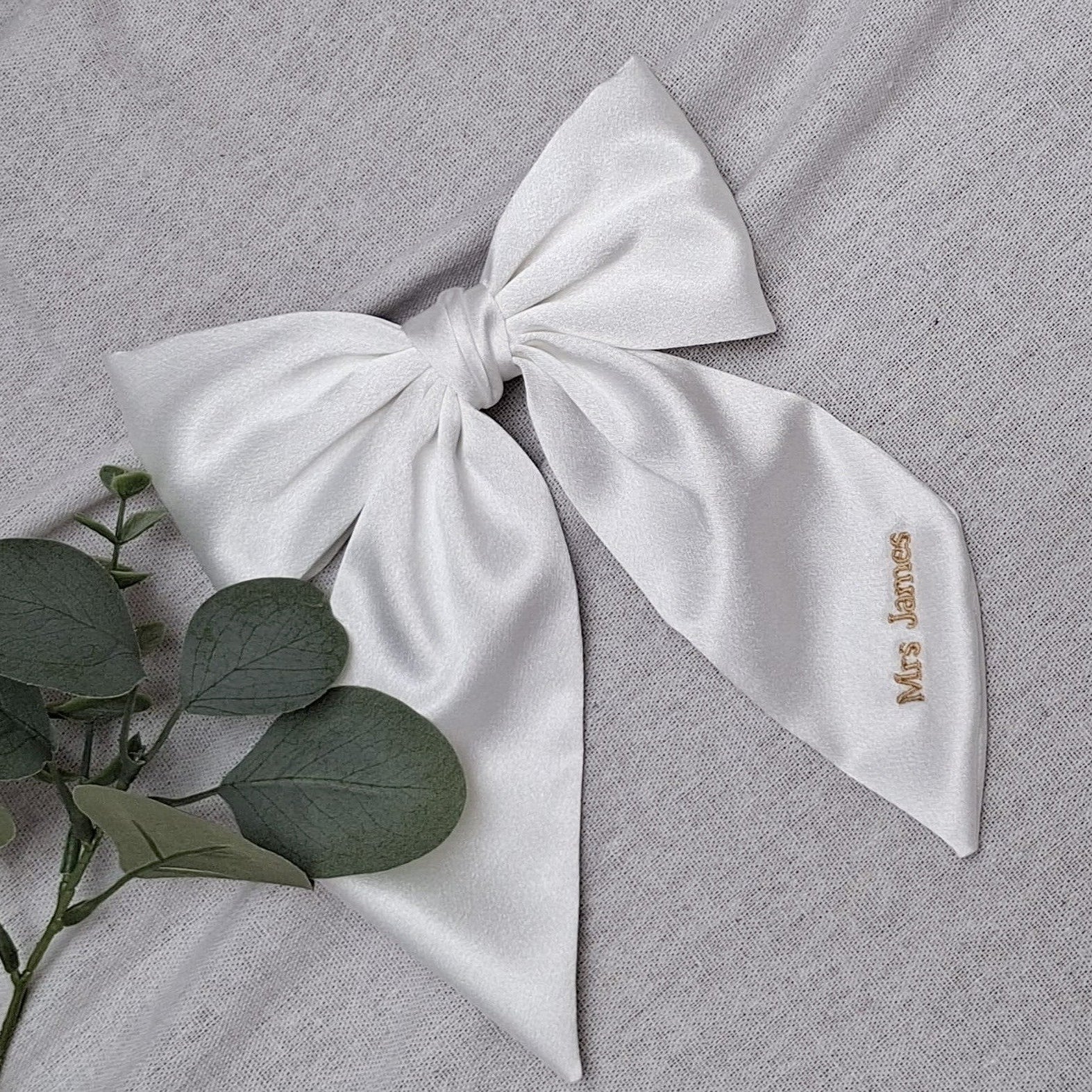 White bow with 'Mrs. James' embroidery on a gray fabric background