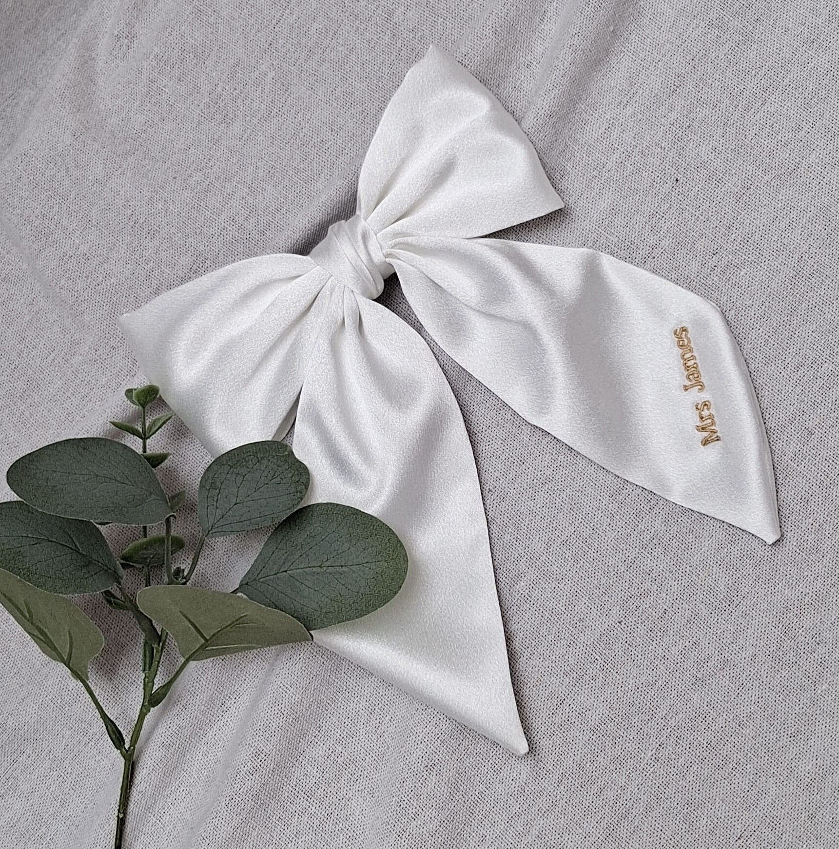 White bow with 'MRS.' embroidery on a gray fabric background