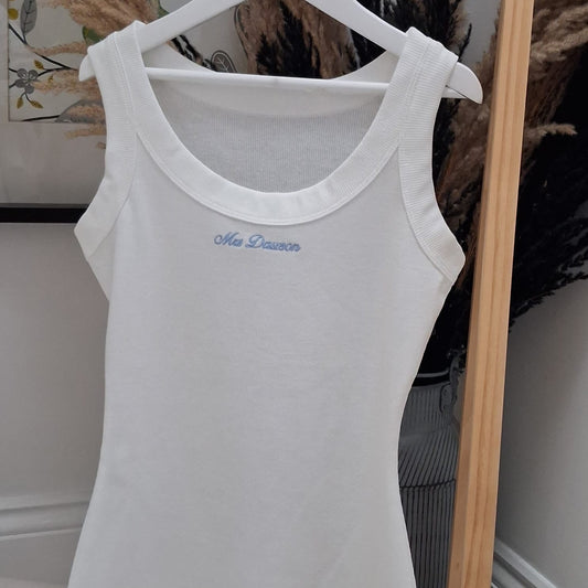 White tank top with blue text on a hanger against a neutral background
