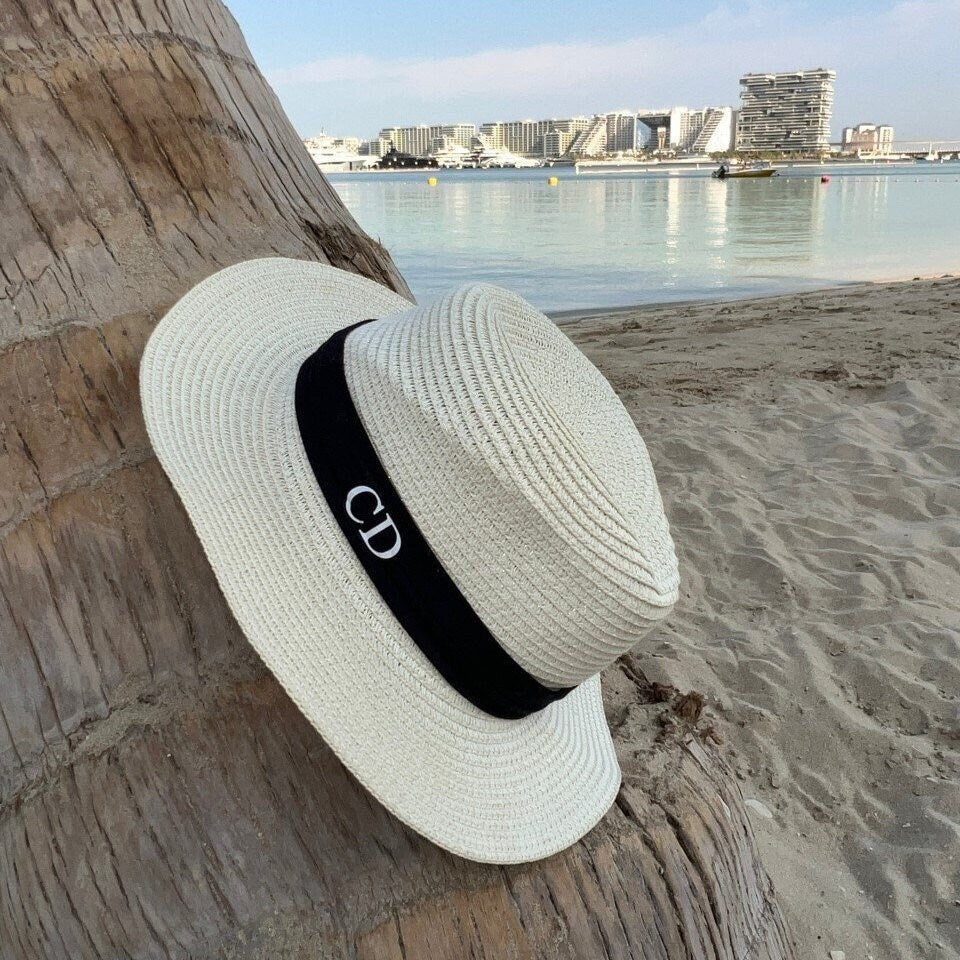 White straw hat with a black band on a wooden log by the beach personalised
