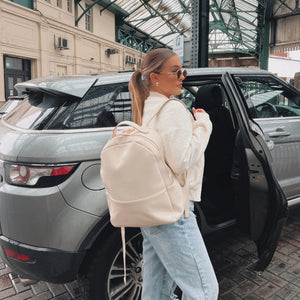 Woman with a beige backpack standing next to an open car door