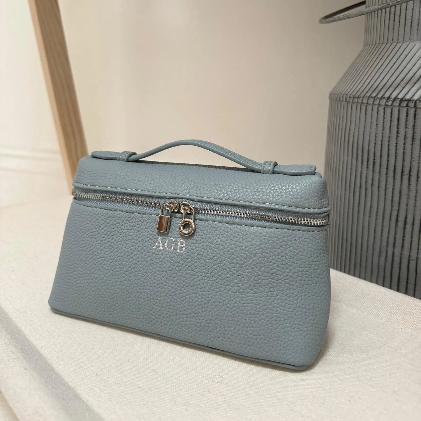 Light blue hand bag with 'AGB' monogram on a neutral background