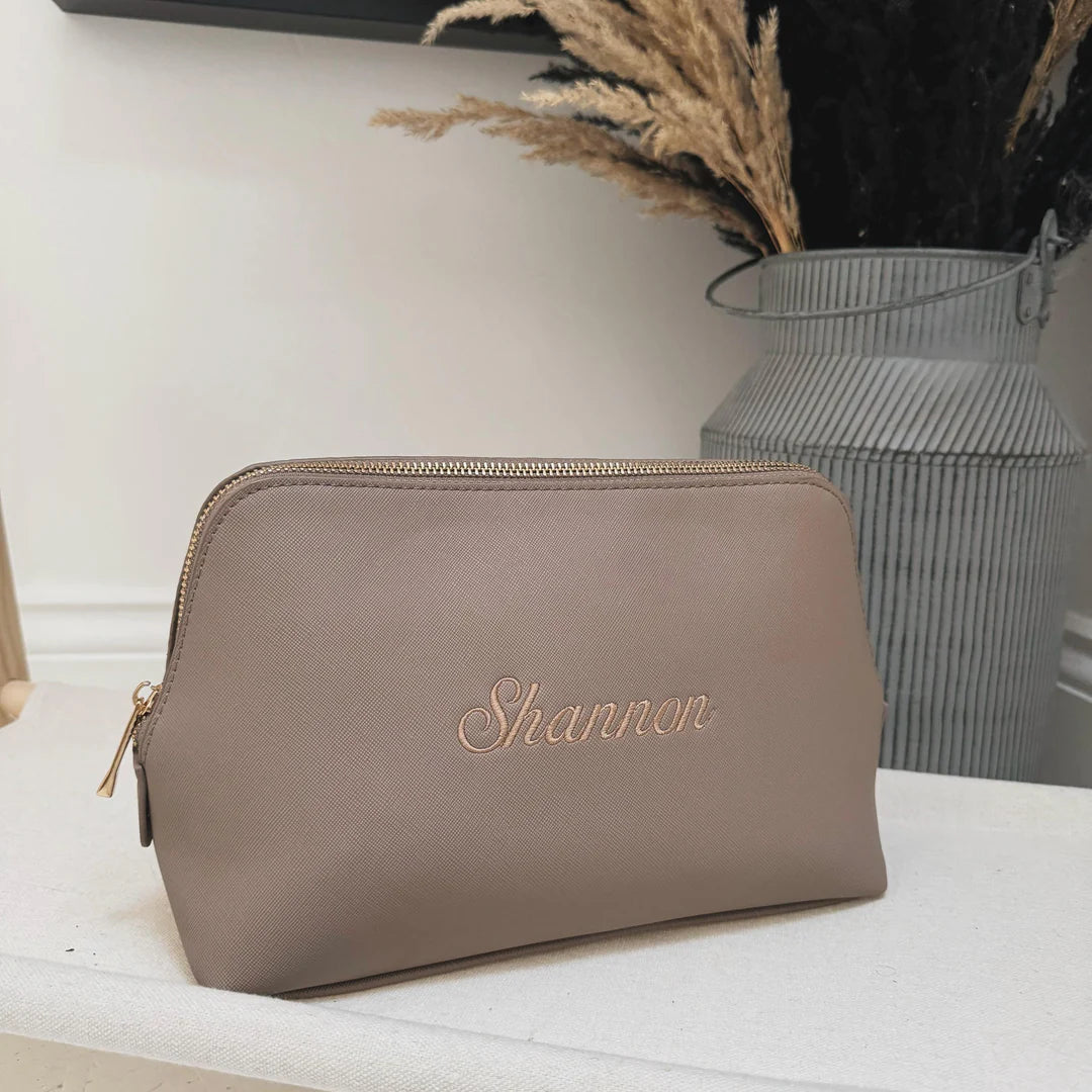Brown pouch with 'Shannon' embroidery on a white surface with a vase in the background