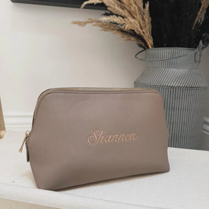 Brown pouch with 'Shannon' embroidery on a white surface with a vase in the background