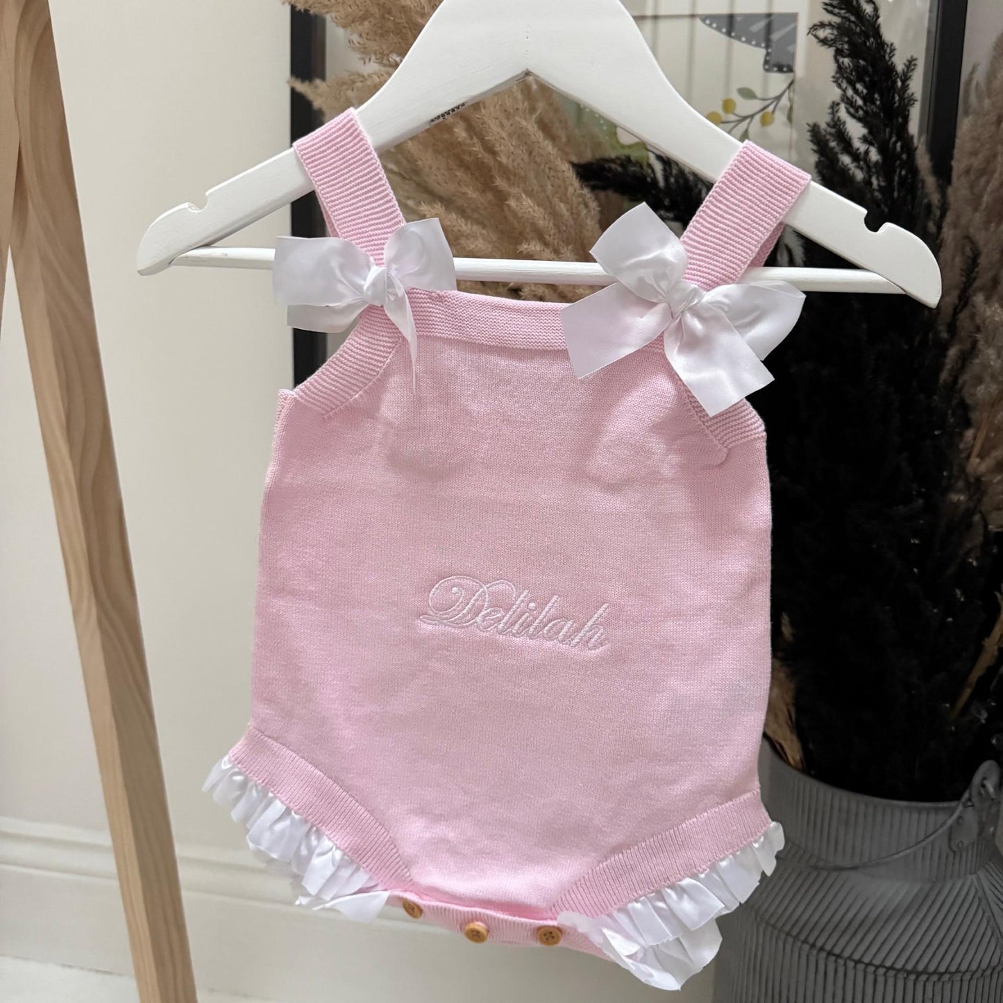 Pink baby romper with white bows on a hanger against a neutral background with personalised name